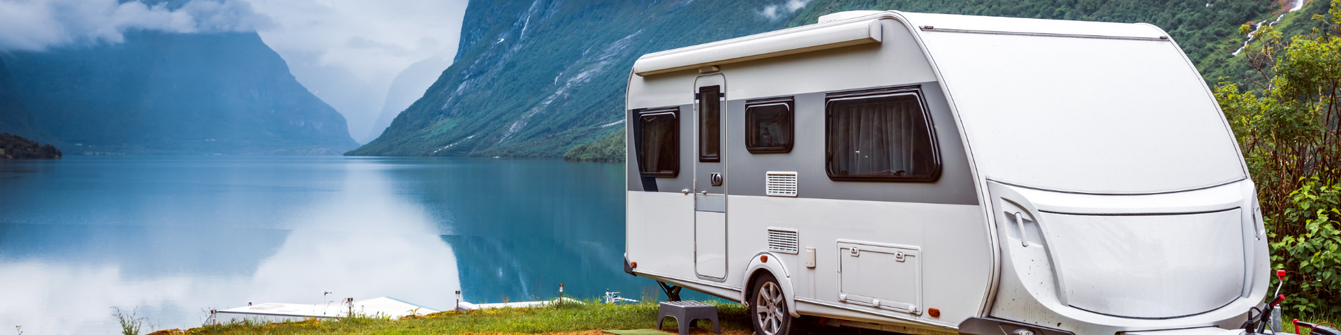 White travel trailer parked by a calm blue lake with snowy mountains in the background