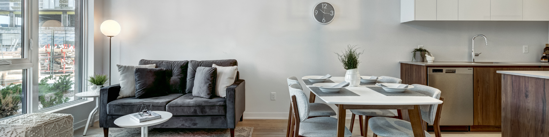 Modern living-dining area with gray sofa, round table, and kitchen in the background