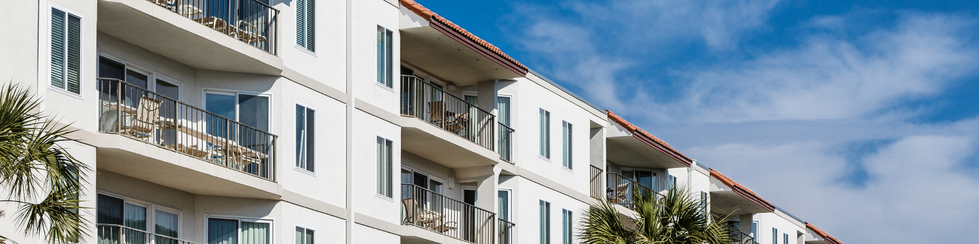 White apartment building with balconies and red-tiled roofs under a clear blue sky