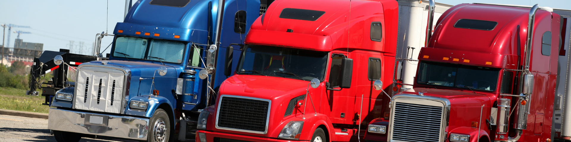 Three semi trucks parked side by side, blue and red cabs in a lot
