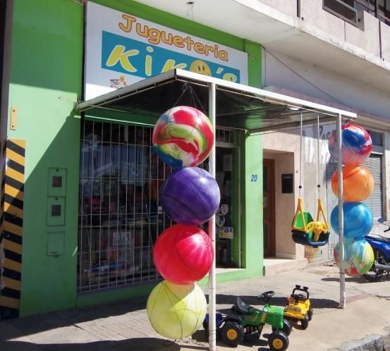Globos de colores frente a la entrada de una tienda de artículos para niños en una calle soleada.