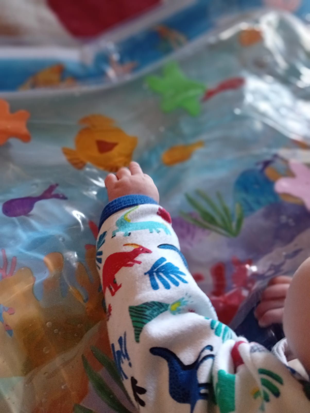 Pie de bebé con pijama estampado de dinosaurios debajo de una colorida manta translúcida.
