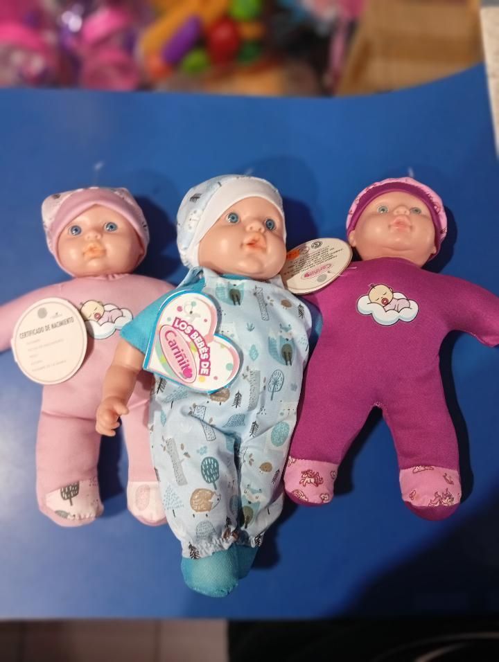 Tres pequeñas muñecas vestidas con ropa rosa, azul y morada, yacían una al lado de la otra sobre una superficie azul.