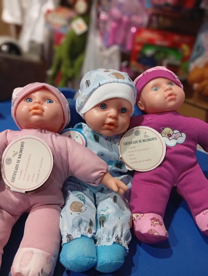 Tres muñecas bebé vestidas con ropa rosa, azul y morada están sentadas juntas sobre una superficie azul.