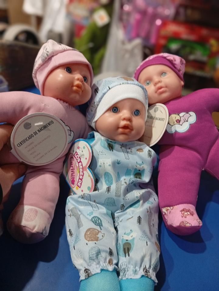 Tres muñecas bebé envueltas en mantas y vestidas con ropa de colores pastel yacen una al lado de la otra sobre una superficie azul.