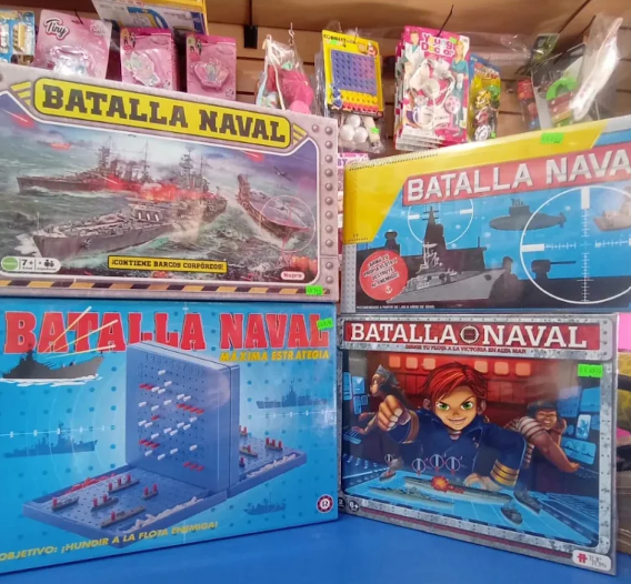 Cajas del juego de mesa “Batalla Naval” apiladas en un estante de una tienda, mostrando barcos de la armada y un empaque azul brillante.