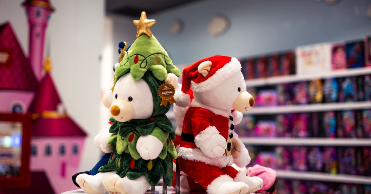 Dos muñecos de peluche navideños, uno con un traje de árbol de Navidad y otro vestido de rojo Papá Noel, expuestos en un estante de una tienda.