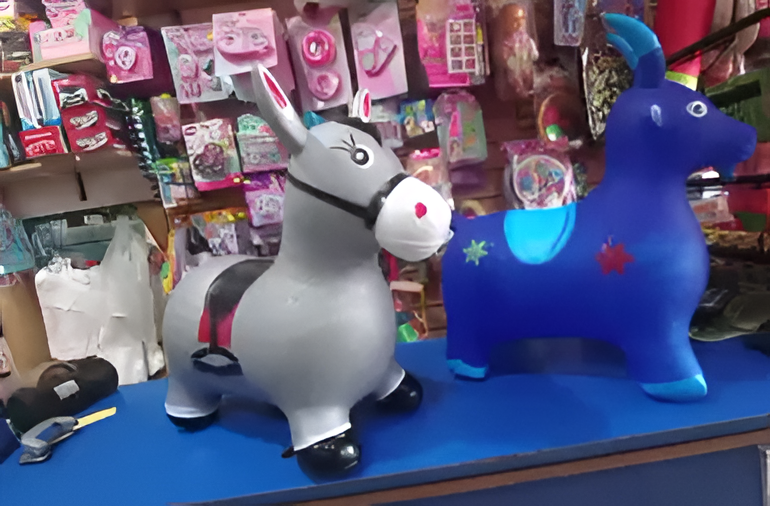 Dos coloridos animales de juguete inflables sobre el mostrador de una tienda, con productos rosas expuestos detrás de ellos.