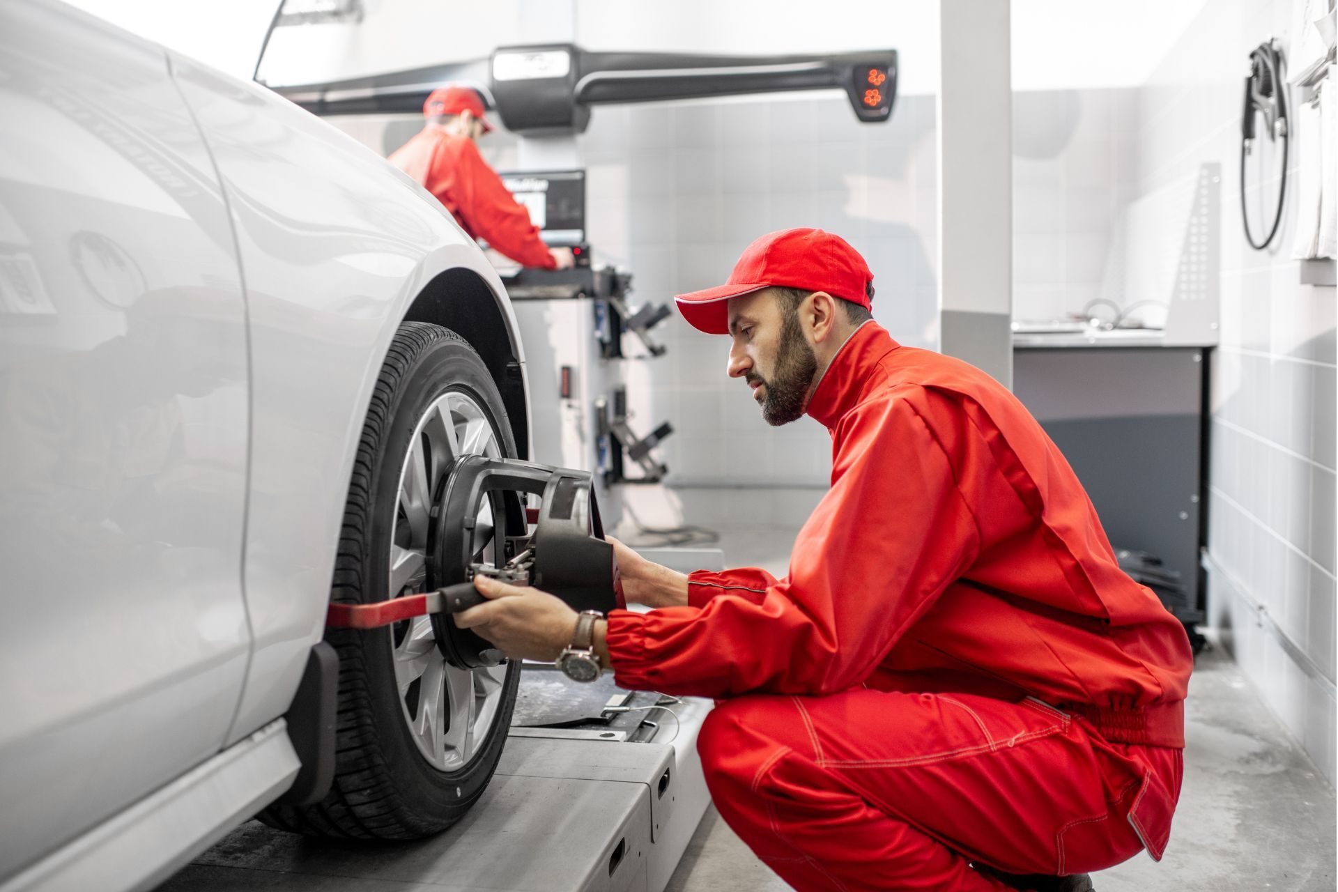A man in a red uniform is working on a car wheel in a garage.