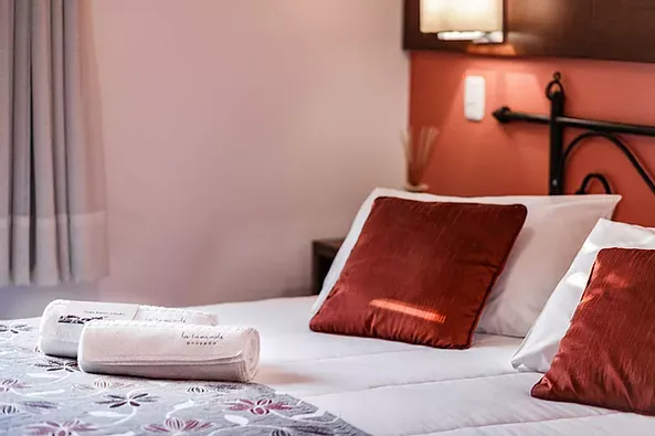 Uma cama com travesseiros vermelhos e lençóis brancos em um quarto de hotel.