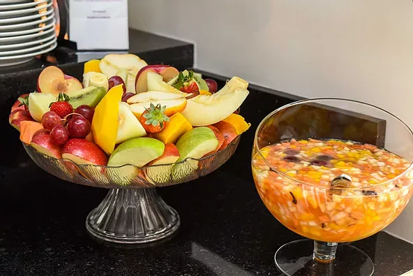 Uma tigela de frutas e um copo de salada de frutas sobre uma mesa.