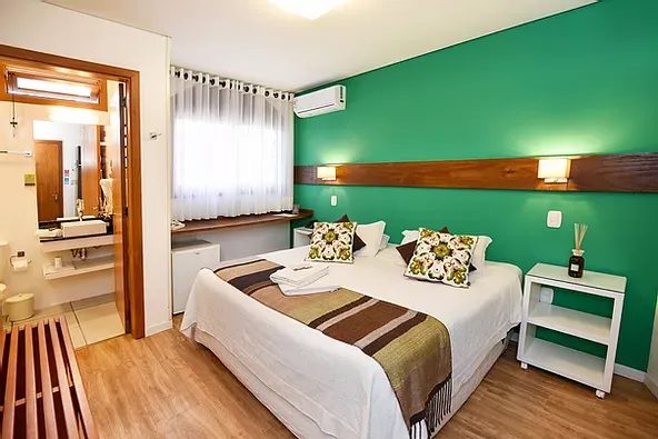 Um quarto de hotel com cama, mesa de cabeceira e paredes verdes.