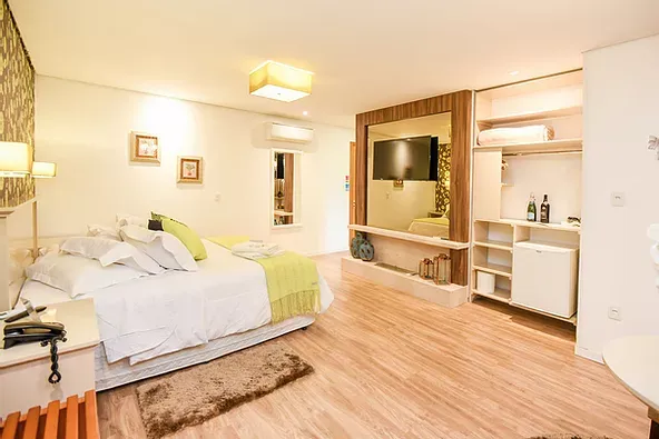 Um quarto de hotel com uma cama grande, televisão e geladeira.