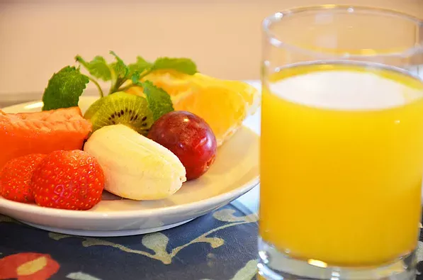 Um prato de frutas e um copo de suco de laranja sobre uma mesa.