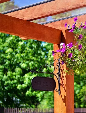 Uma pérgula de madeira com flores roxas e uma placa de boas-vindas pendurada nela.