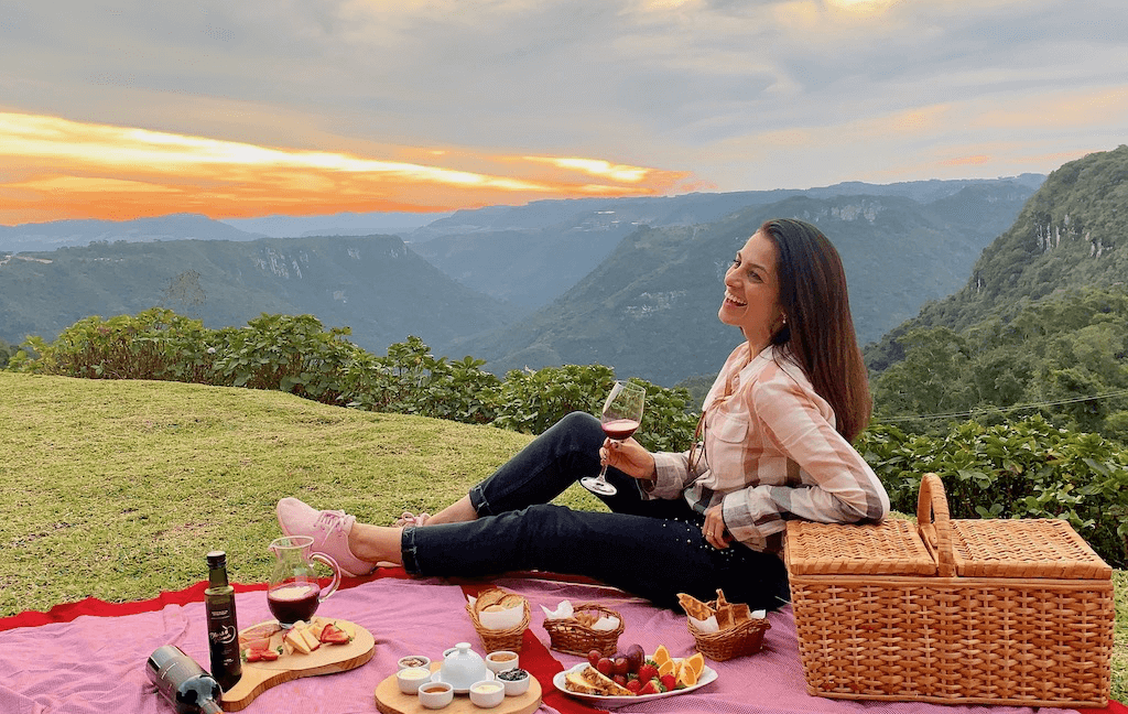 Uma mulher está sentada em uma toalha de piquenique segurando uma taça de vinho.