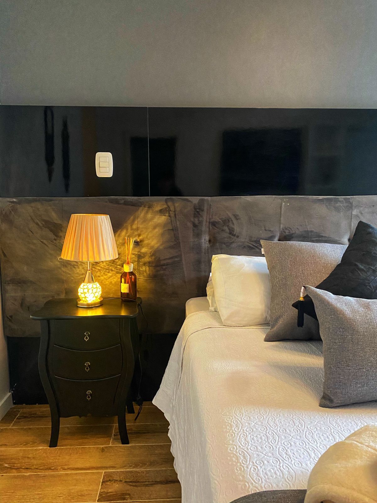 Um quarto com cama, mesa de cabeceira, abajur e televisão.