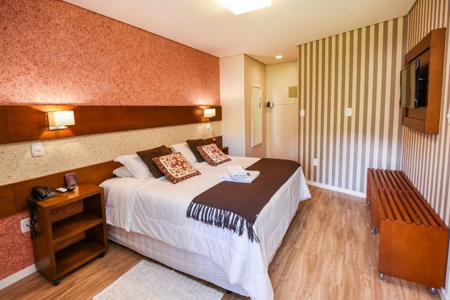 Um quarto de hotel com cama, mesa de cabeceira, televisão e papel de parede listrado.