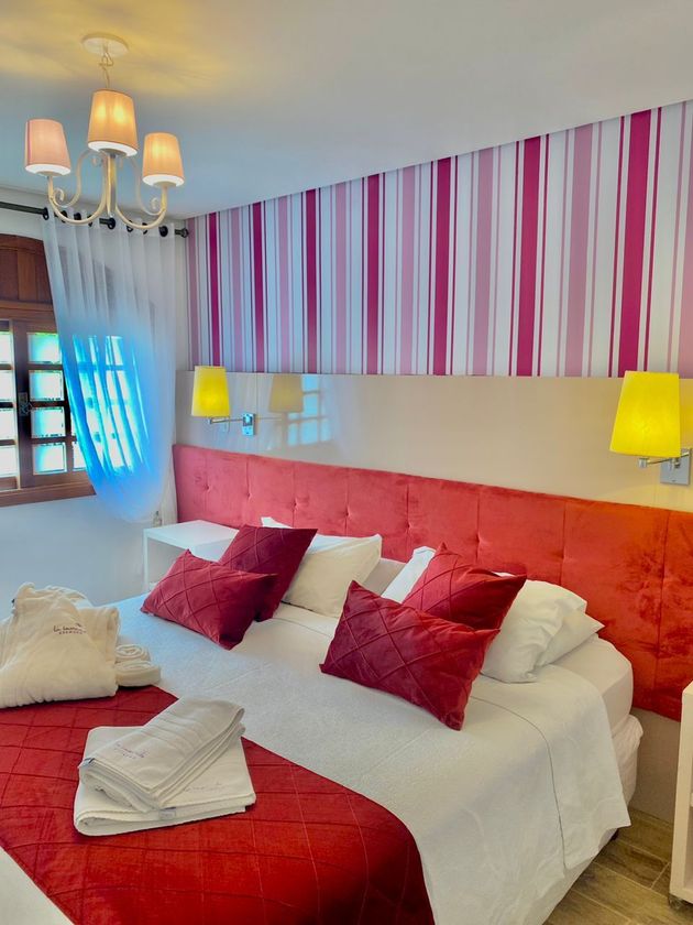 Um quarto com cama vermelha e papel de parede listrado
