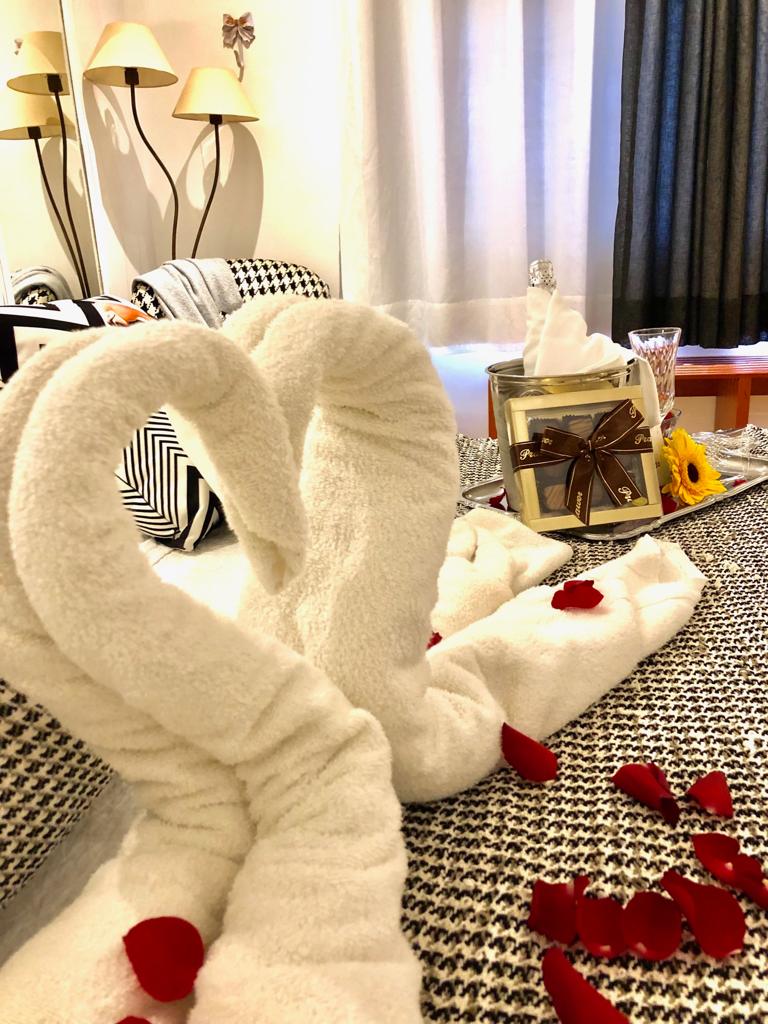 Uma cama com uma toalha em forma de coração e pétalas de rosa.