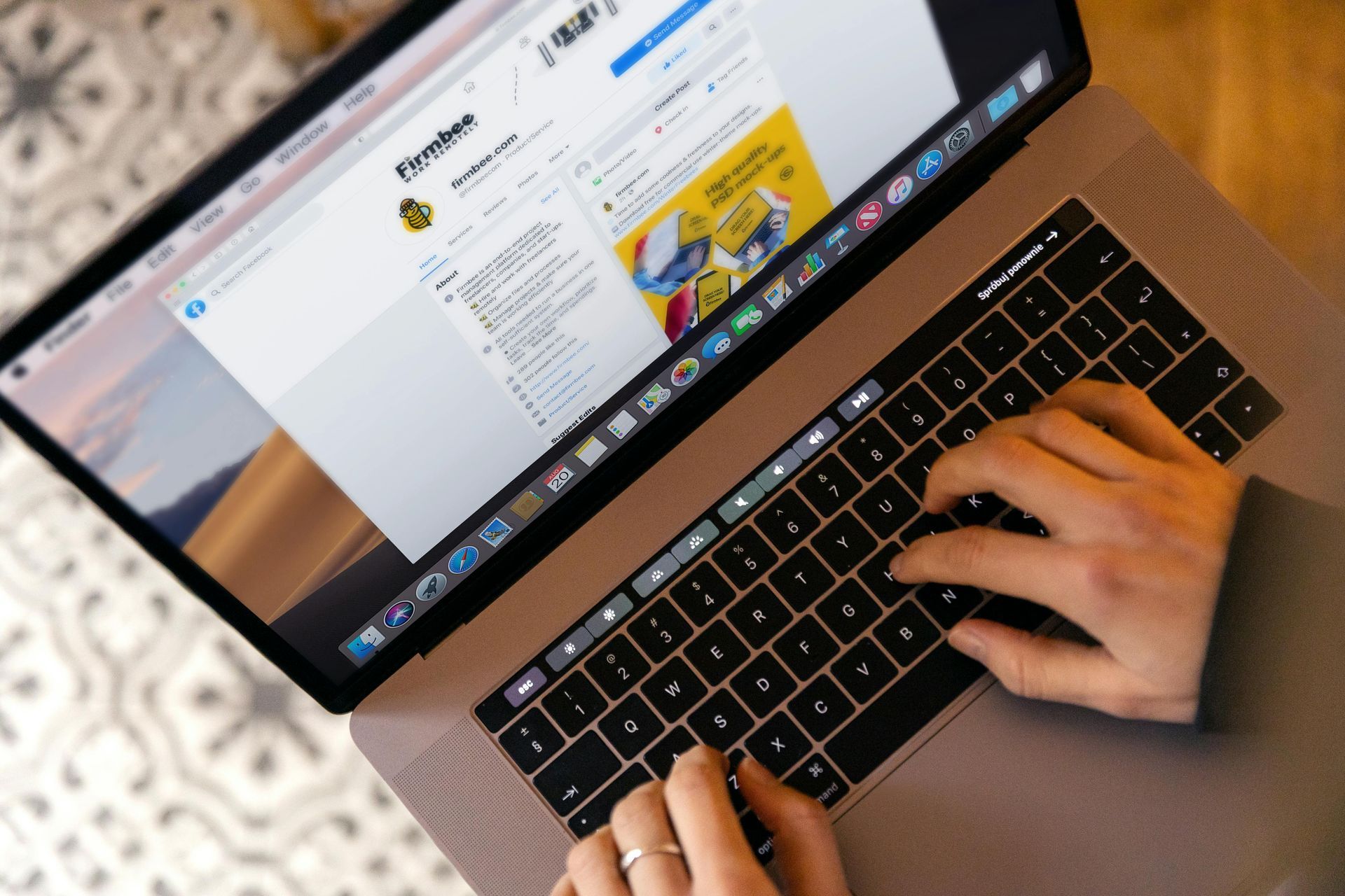 A person is typing on a laptop with a facebook page on the screen.