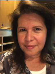 A portrait of a person with dark hair, wearing a patterned floral top, looking directly at the camera.