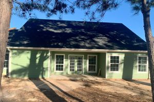 Green house with dark roof, front porch, and two garage doors under trees in daylight