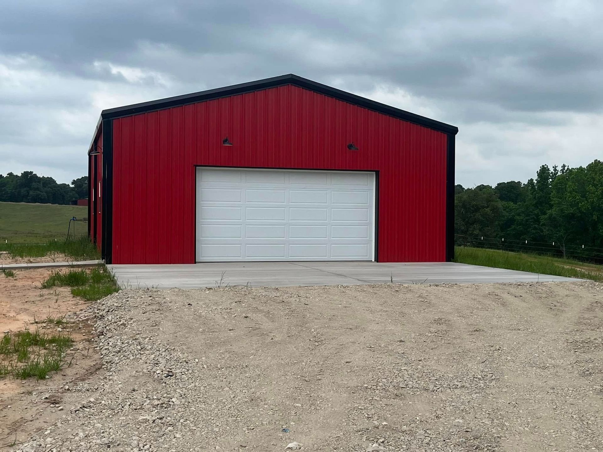 Red metal barn with a white garage door on a gravel lot under a cloudy sky.