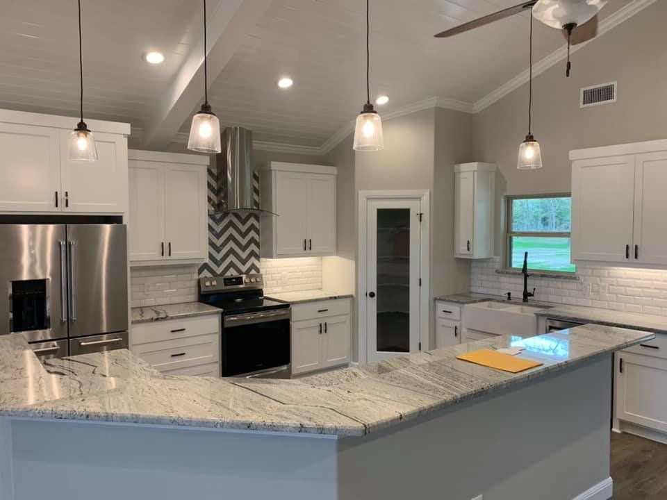 Modern kitchen with white cabinets, granite island, stainless steel appliances, and chevron tile backsplash