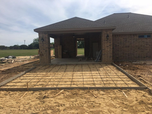 Partially built brick house with a covered porch and unfinished concrete patio in front