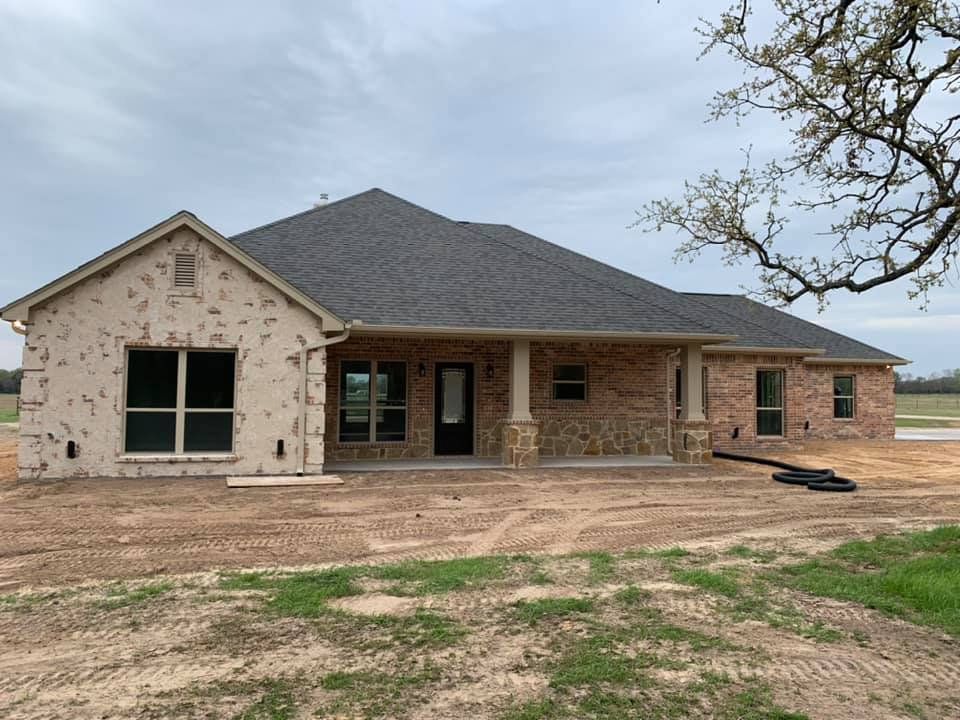 Single-story brick and stone house under construction with a covered front porch and bare dirt yard.