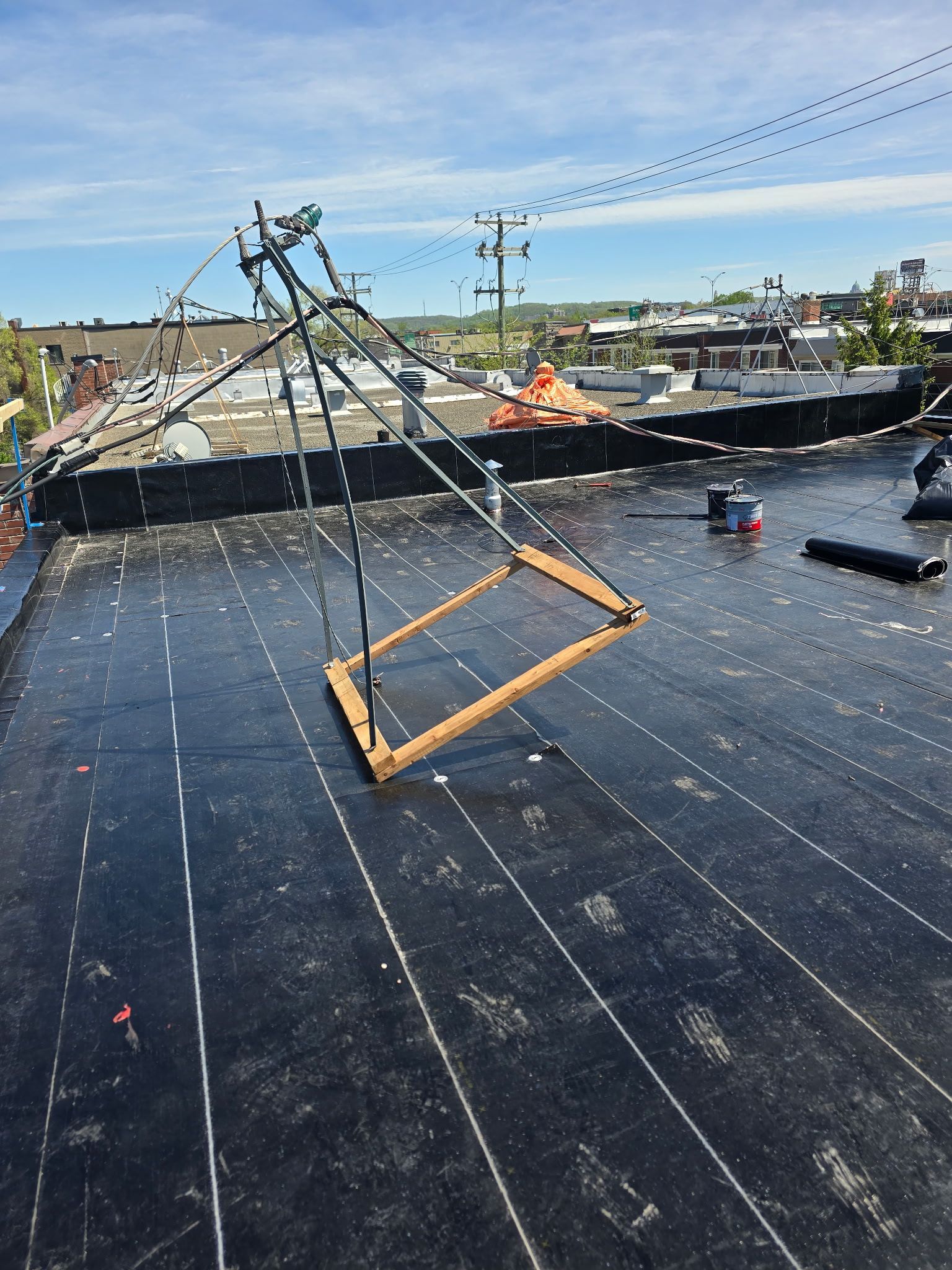 Construction de toiture avec étanchéité noire, charpente en bois suspendue et ouvriers au loin