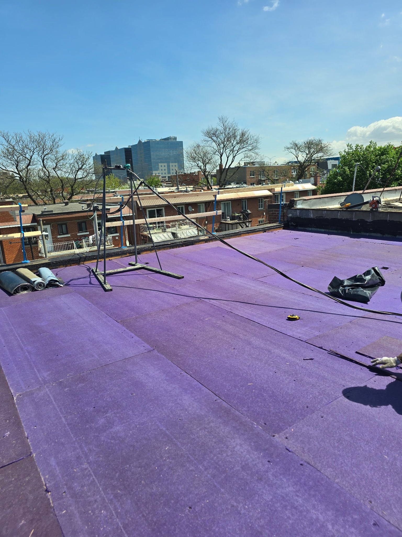 Toit violet avec des câbles et des équipements sous un ciel bleu clair, avec des arbres et des bâtiments au loin.