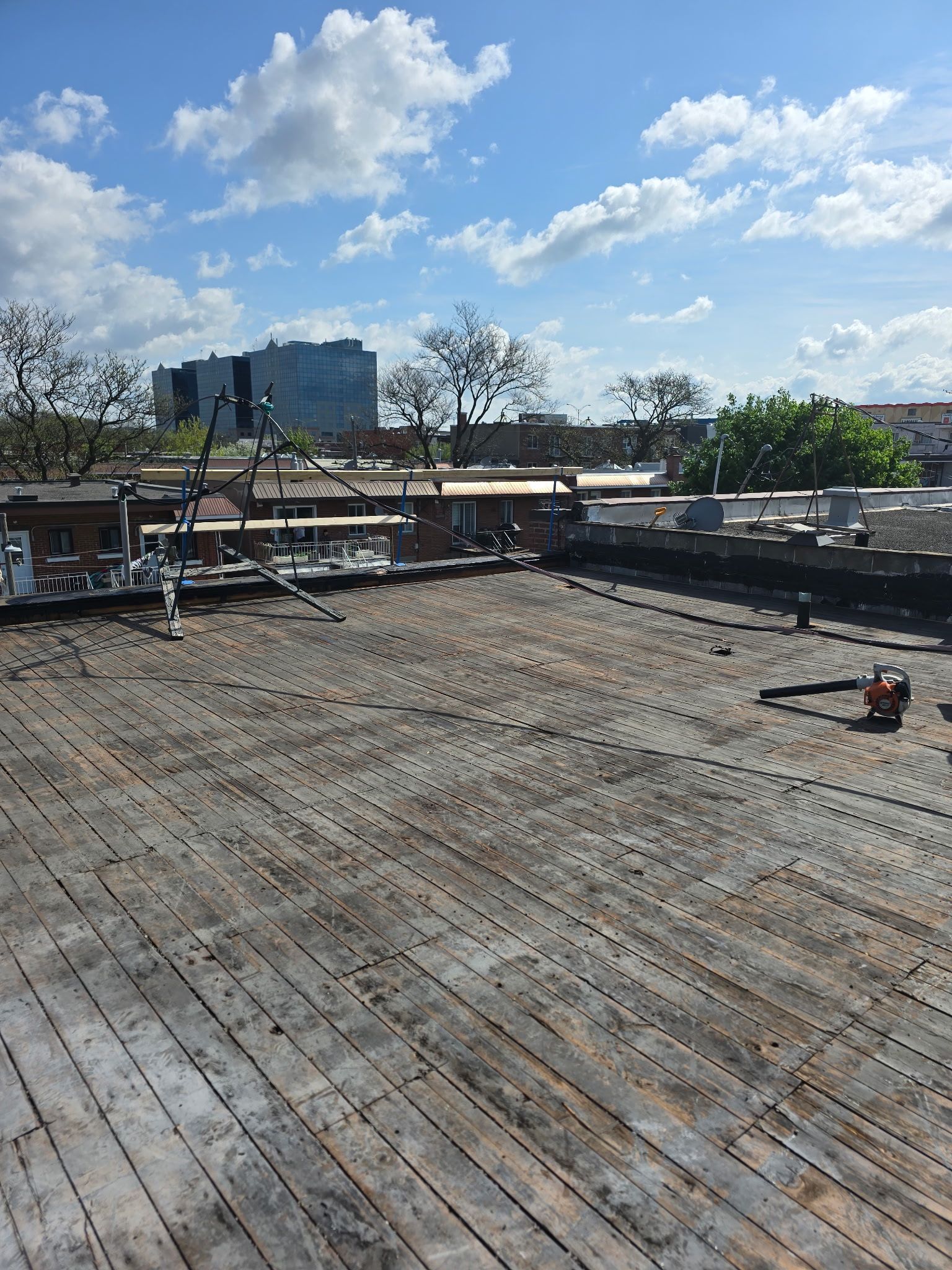 Terrasse sur le toit en construction avec poutres en bois apparentes, outils et vue sur la ville sous un ciel bleu.