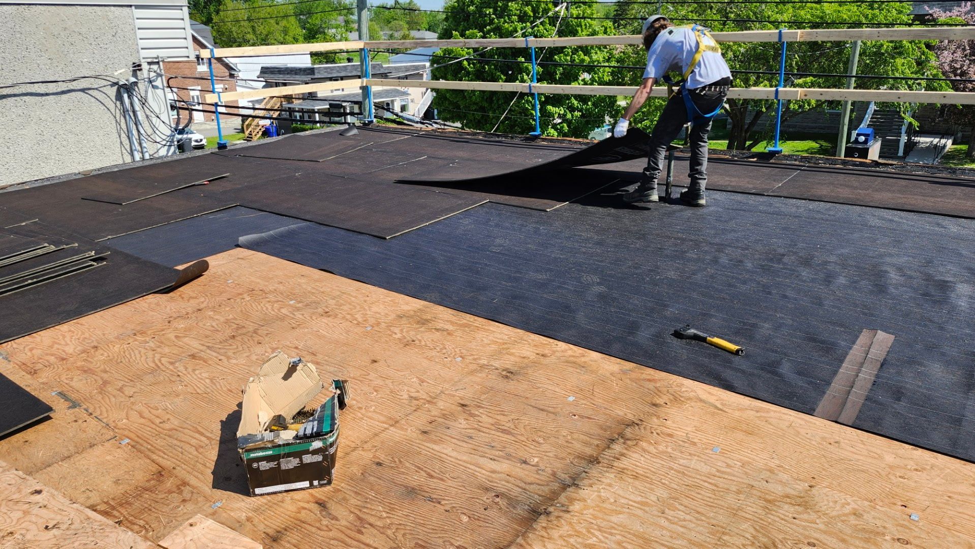 Des ouvriers installent une membrane d'étanchéité noire sur un toit plat, outils et matériaux étalés sur le dessus.