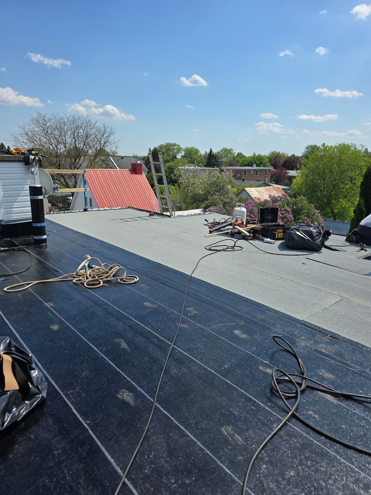 Toiture en réparation avec sous-couche foncée, ouvriers, outils et ciel bleu en arrière-plan