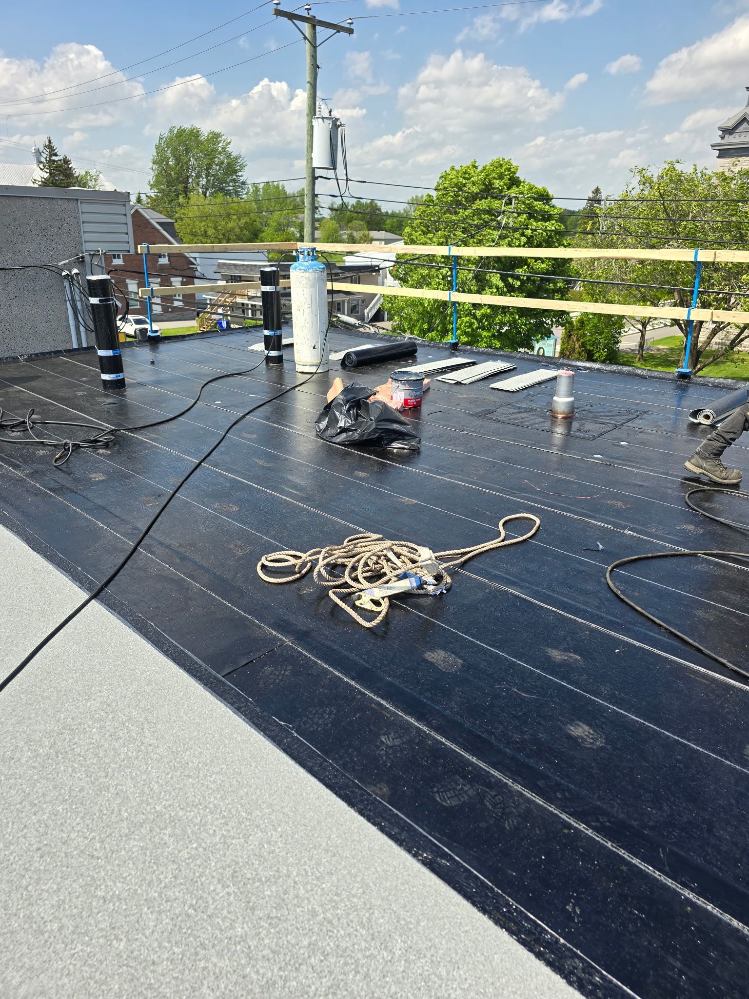 Toiture avec panneaux solaires noirs, boîtier électrique et câble enroulé sous un ciel partiellement nuageux.