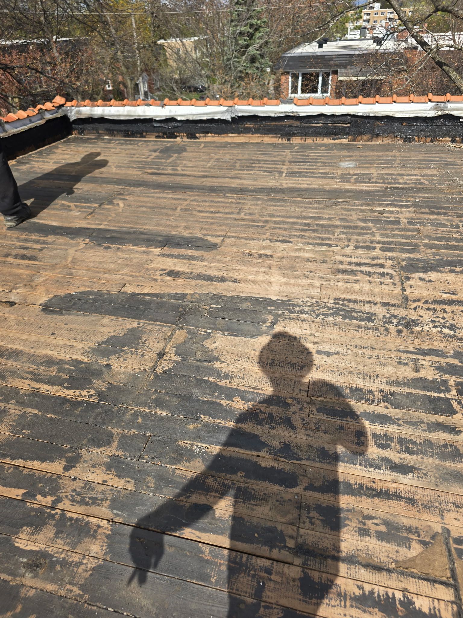 Toit plat avec une toiture noire patinée et l'ombre d'une personne au premier plan.