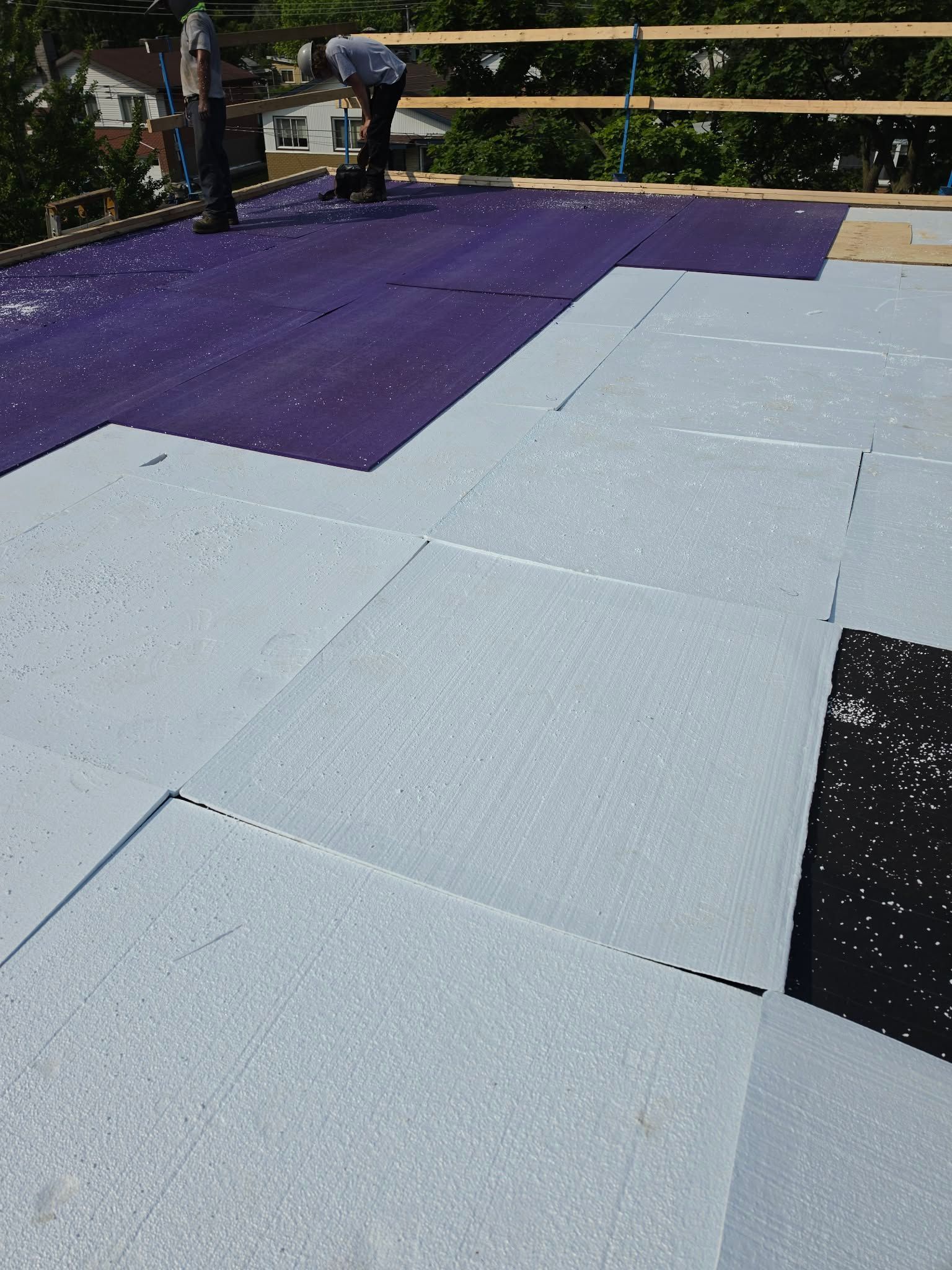 Des ouvriers installent des tuiles violettes et blanches sur un toit près d'une clôture en bois