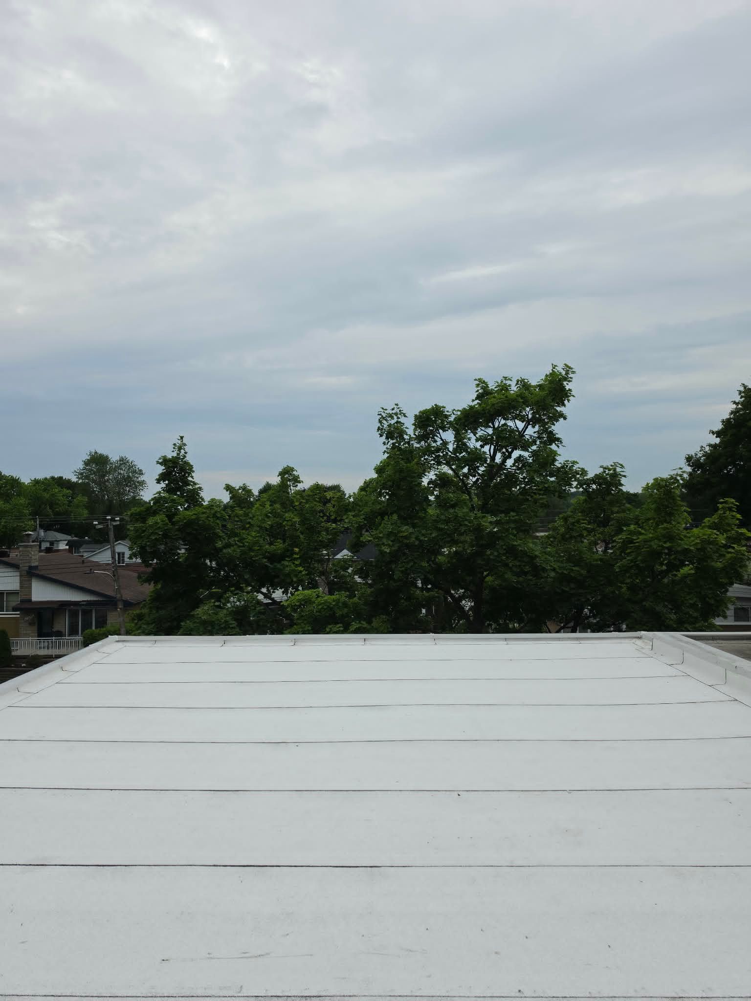 Ciel nuageux au-dessus d'un toit blanc avec des arbres et des maisons au loin.