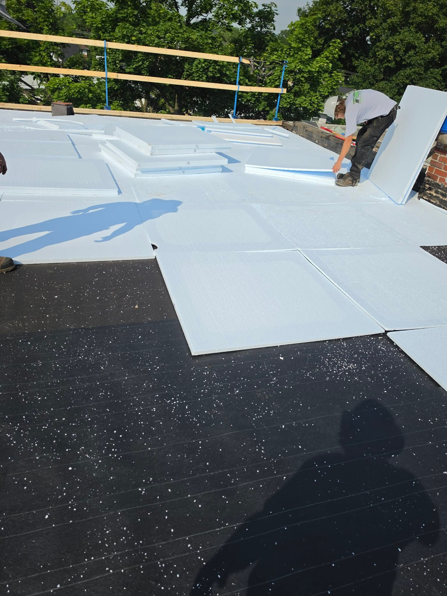 Toiture en construction avec panneaux isolants bleus, sous-couche noire et garde-corps en bois à l'extérieur