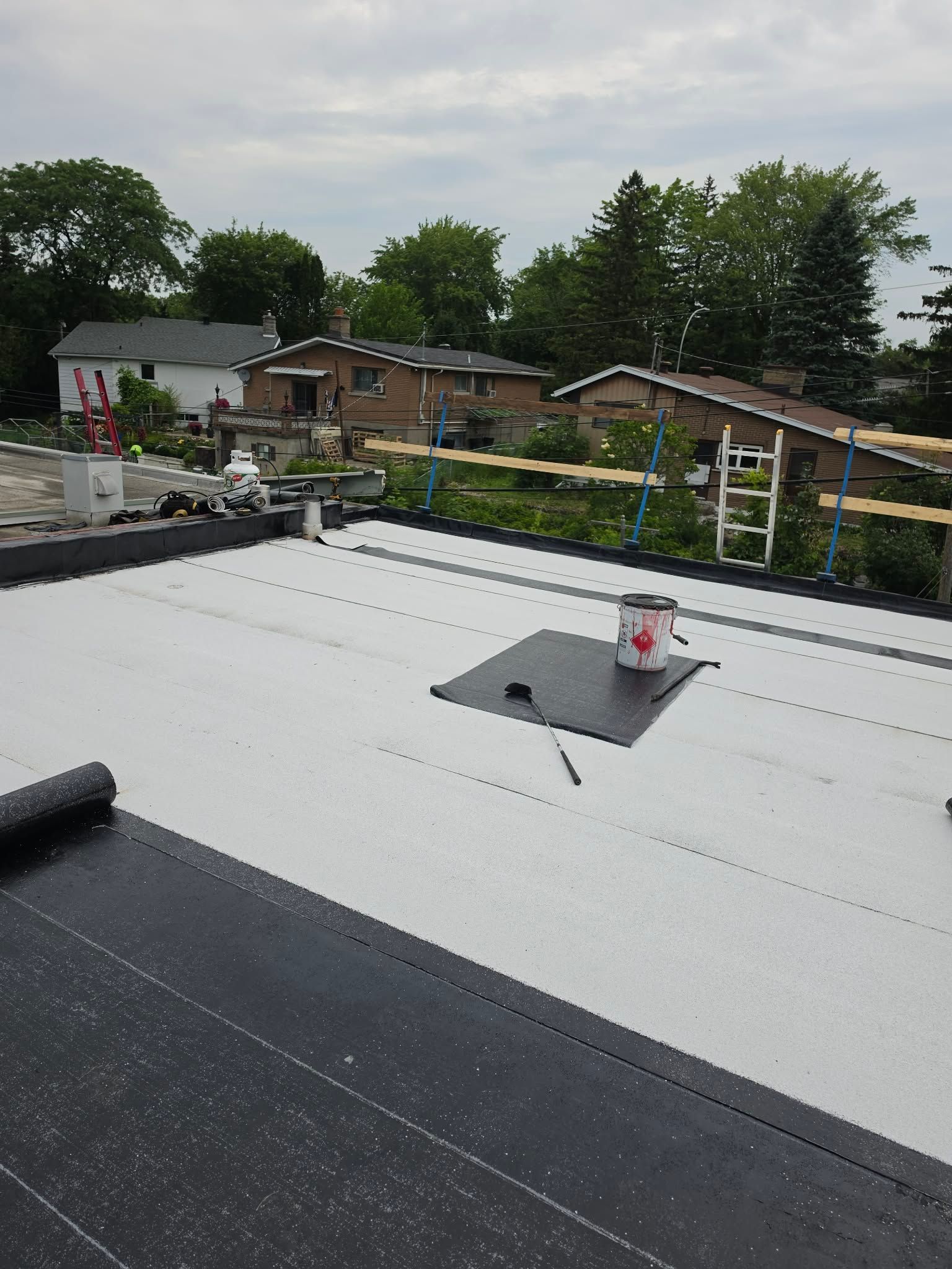 Toit plat recouvert d'une membrane blanche et muni d'une petite ouverture d'aération, donnant sur des maisons et des arbres sous un ciel couvert.