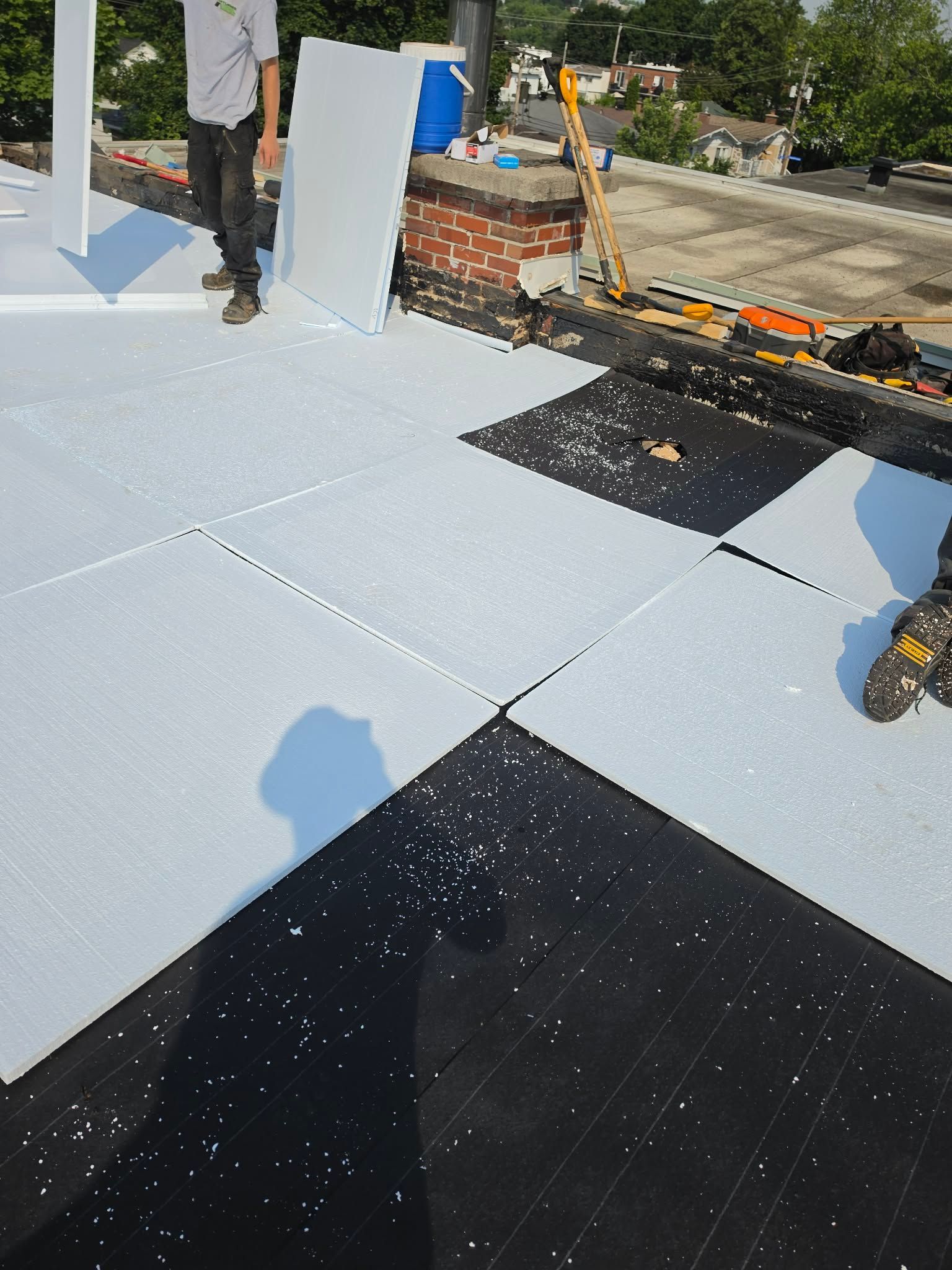 Des ouvriers installent des tuiles de toiture gris clair et noires sur un toit plat.