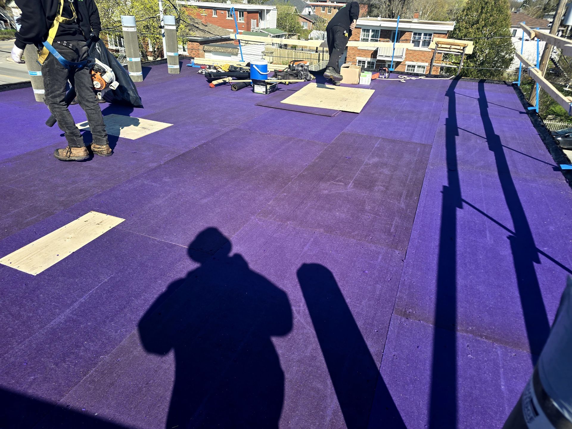 Des ouvriers installent une sous-couche de toiture violette sur un toit plat à l'aide d'outils et d'équipements de toiture.