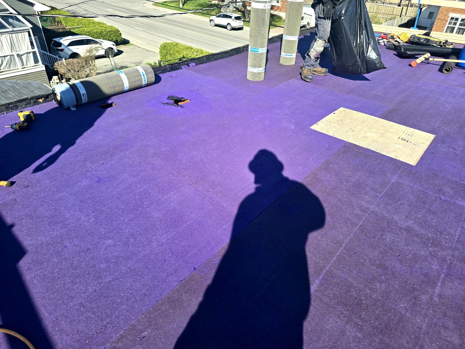 Terrasse sur le toit recouverte de moquette violette, avec des ombres, des arbres et une route visible au-delà du bord.