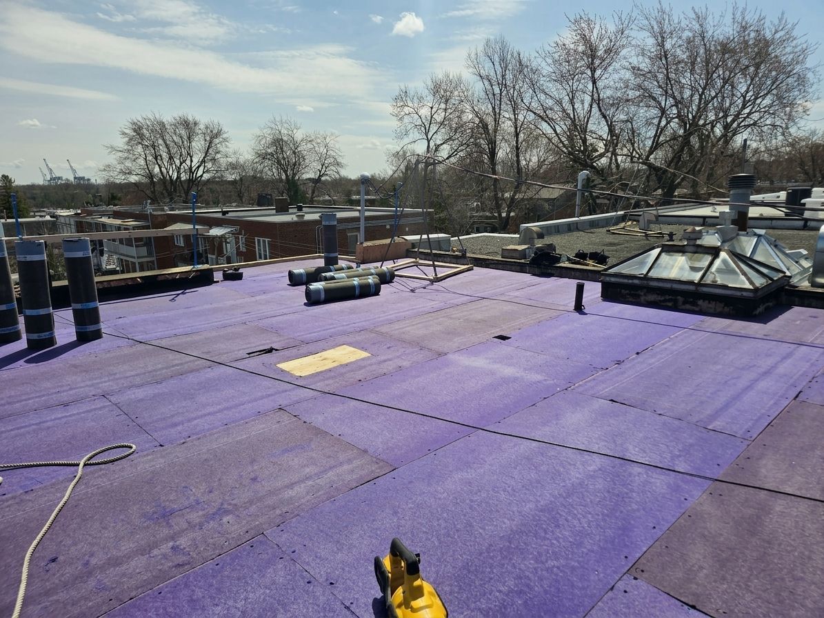 Toit plat recouvert d'une sous-couche violette, avec des équipements de toiture et des arbres en arrière-plan.