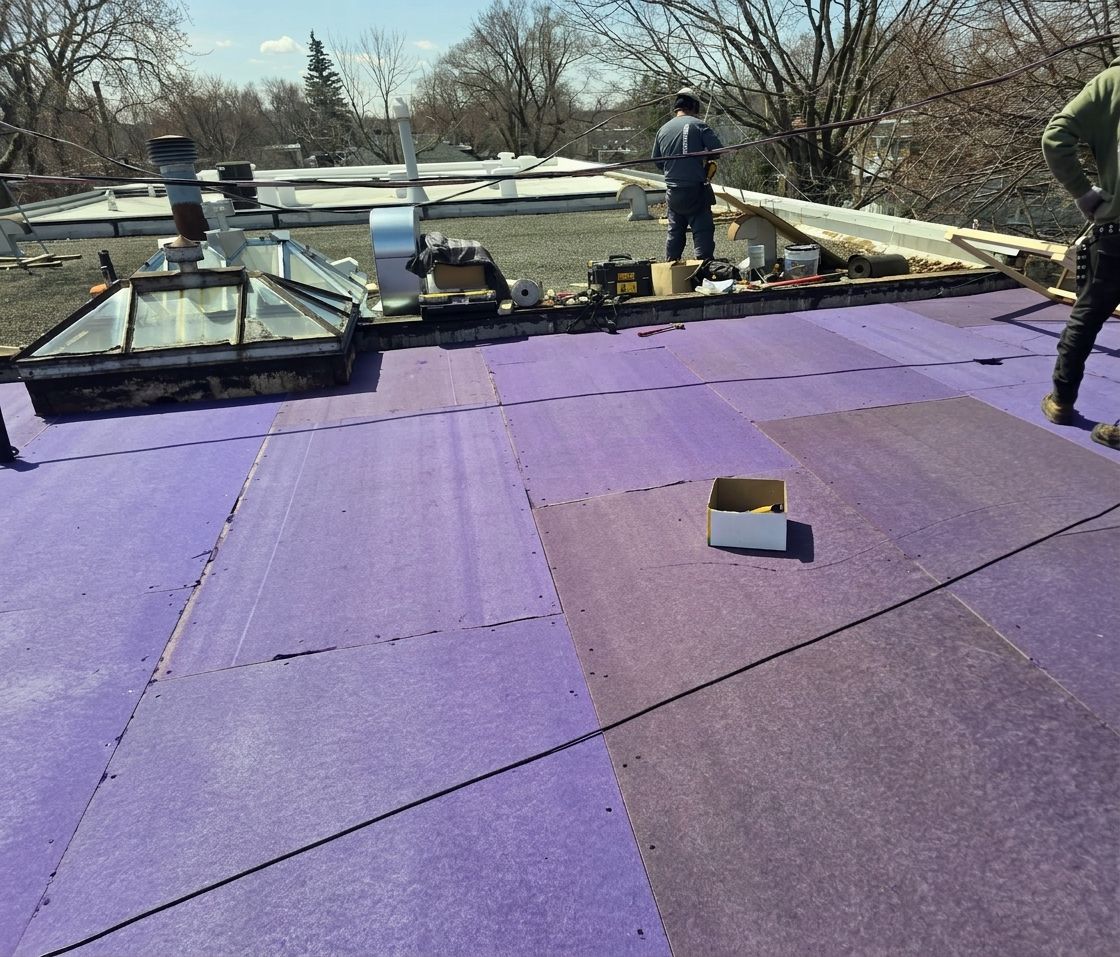 Des ouvriers installent une membrane d'étanchéité violette sur un toit plat en construction.