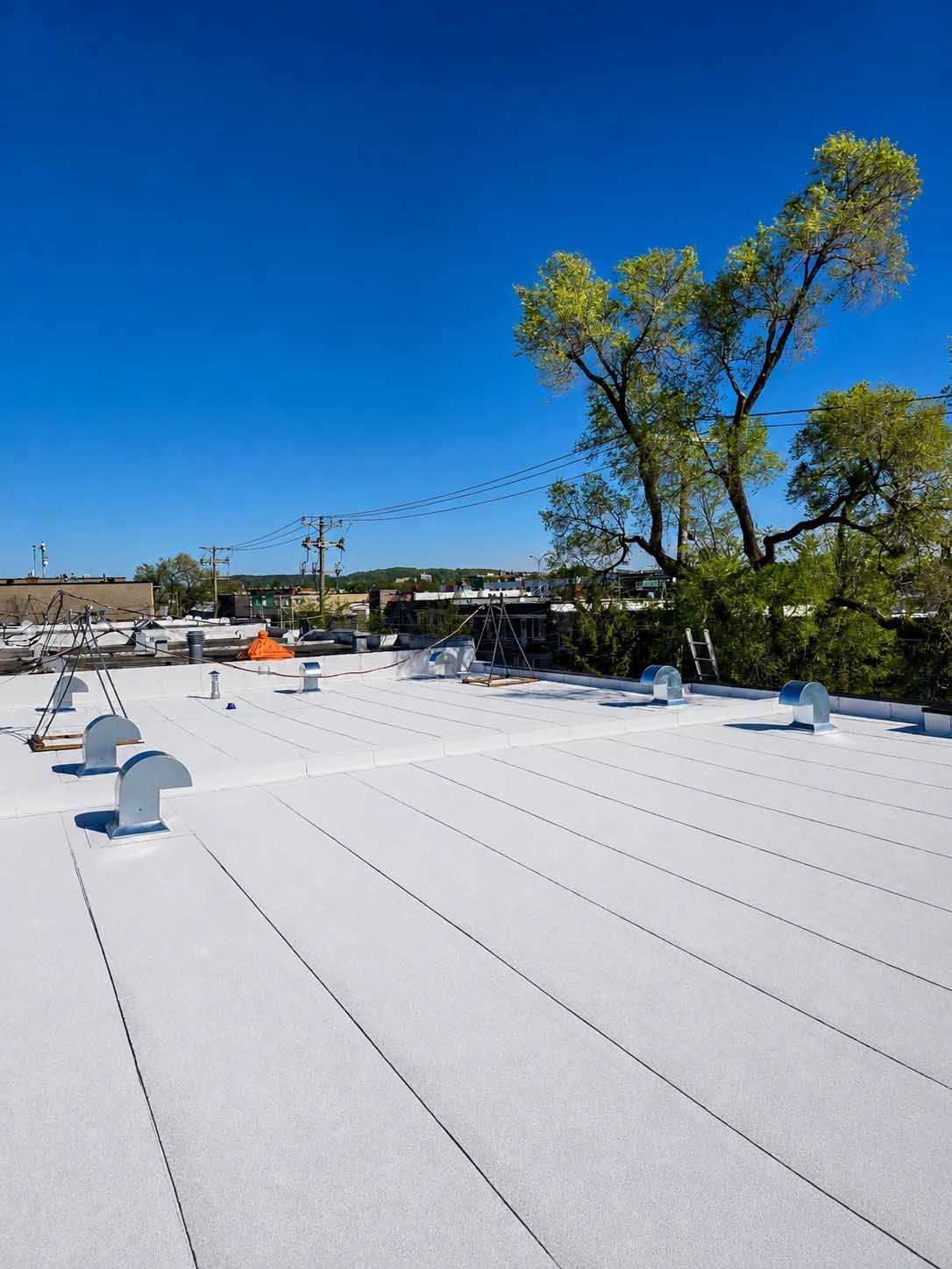 Toit plat blanc avec des aérations sous un ciel bleu clair, avec des arbres et des bâtiments au loin en arrière-plan