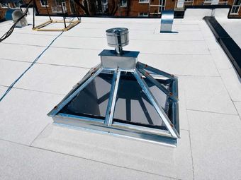 Puits de lumière métallique avec une petite ouverture d'aération sur un toit plat blanc, avec des bâtiments en arrière-plan