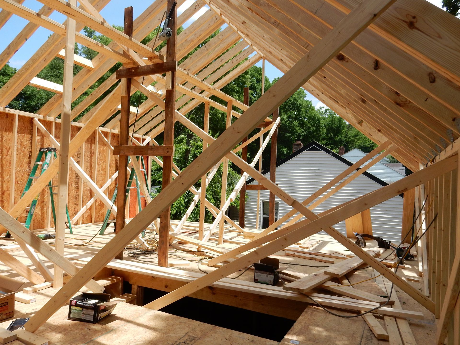 Wooden roof trusses under construction at a house build site, with sunlight and a ladder.